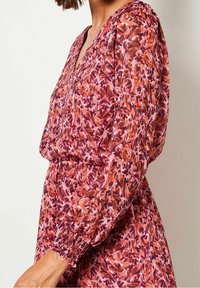 Kukallinen mekko pinkin ja oranssin sävyissä, joissa on pitkät, tiukat hihat ja rypytetty vyötärö. V-p.tyylinen design ja virtaava kangas.