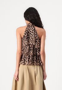 Haut à bretelles en imprimé léopard avec des volants superposés, dans des tons beiges, et un lien autour du cou. Le tissu semble doux avec un drapé léger.