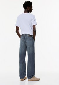 Ljusgrå t-shirt med kort ärm, kombinerad med blå jeans i avslappnad passform med en standard femfickdesign och ett svart bälte.