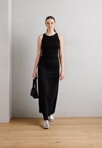 Svart tettsittende tank topp kombinert med et langt svart skjørt. Antrekket har glatt stoff og enkelt design. Sølvfargede sko og en liten svart veske.