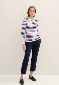 Langärmliges gestreiftes Oberteil in Weiß mit marineblauen, pinkfarbenen und hellblauen horizontalen Streifen. Kombiniert mit marineblauen Hosen und schwarzen Loafers. Schlichtes Design.