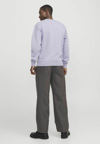 Licht paarse sweatshirt met lange mouwen, geribbelde manchetten en zoom, gecombineerd met losse grijze broeken en zwarte schoenen.