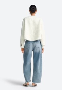 Balta teksturēta īsa jaka ar apaļu kakla izgriezumu, kopā ar gaiši zilām plaša piegriezuma džinsa biksēm ar nejauši izplūdušiem apakšmalām un diviem aizmugures kabatām.