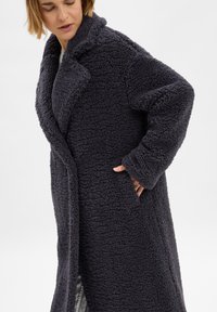 Donkergrijze oversized jas van fluffy, gestructureerde stof. Voorzien van een notch-kraag en zijzakken. Lange mouwen met opgerolde manchetten.