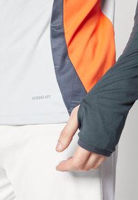 Aerodynamic athletic shirt featuring a gray base, orange and dark blue accents, textured panels, and thumbholes at the cuffs.