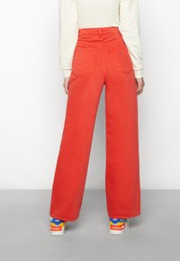 Rote weite Jeans mit hohem Taillenbund und hinteren Taschen. Kombiniert mit bunten Turnschuhen. Glattes, strapazierfähiges Denim-Material.