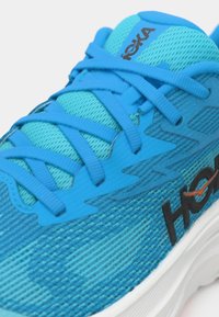 Modrá sportovní bota s texturovaným síťovaným svrškem, ladícími tkaničkami a černým logem. Vyznačuje se výrazným polstrováním a vlnícími se designovými prvky.