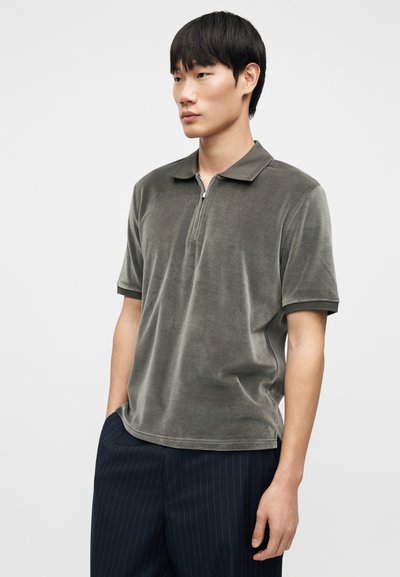 Μπλούζα πόλο με κοντά μανίκια σε ελιά πράσινο, κατασκευασμένη από απαλό, υφασμάτινο ύφασμα με υφή, με φερμουάρ στο πέτο και κλασικό γιακά. Παντελόνι με ναυτικό ρίγα.