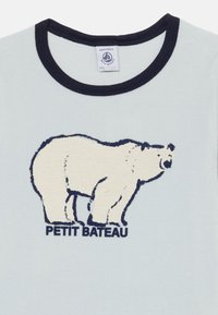 Light blue t-shirt with a navy ribbed collar. Features a textured white polar bear graphic and "PETIT BATEAU" text below in navy.