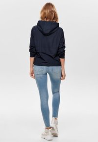 Navy hooded jacket with a sleek design, paired with light blue skinny jeans and white sneakers. Smooth fabric with contrasting color accents.