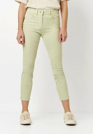 Light green, high-waisted jeans with a slim fit and cropped length, featuring a front button and zip closure, styled with beige sneakers.