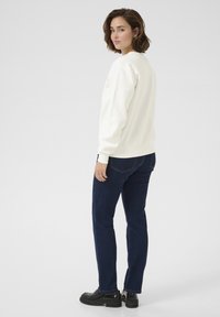 White sweatshirt with long sleeves and ribbed cuffs, paired with dark blue jeans and black shoes. Simple, relaxed fit design.