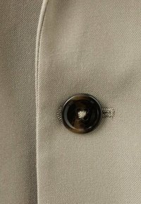 Beige fabric with a smooth texture features a large dark brown button with a subtle sheen and four holes, attached with a thread loop.