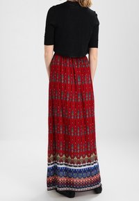 Sukienka maxi z czerwonej tkaniny z niebiesko-białymi wzorzystymi akcentami. Dopasowany czarny krótki top z krótkimi rękawami. Gładka tekstura.