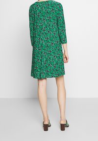 Vihreä kukkakuvioinen mekko, jossa on kolmevartiset hihat, löysä istuvuus ja pyöreä pääntie. Mekossa on eloisa lehti- ja pienikukkakuvio. Ruskeat blokkikorkokengät.