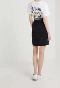 Jupe noire au toucher lisse, avec une taille élastique et deux poches latérales. Assortie à un t-shirt blanc arborant un texte noir audacieux et un design graphique.