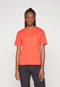 T-shirt à manches courtes en coton orange vif avec un col rond. Présente un petit logo gris foncé sur le côté supérieur gauche de la poitrine.