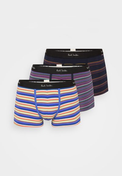 Trois paires de sous-vêtements pour hommes à rayures. La paire de devant présente des rayures bleues, crème et rouges ; les paires de derrière sont sombres avec des motifs de rayures variés.
