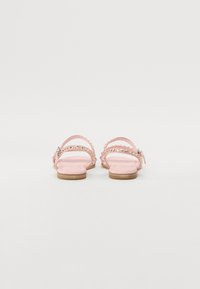 Pink flat sandals with clear straps, decorative studs, and scalloped edges. Wooden sole with smooth texture and minimal design.