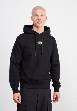 Sudadera negra con un bolsillo canguro frontal, cordones y un pequeño logo blanco en el pecho. El material parece suave y texturizado.