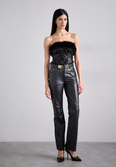 Sort palietteret strapless top med fjerkant, parret med tætsiddende sorte læderbukser og højhælede sorte sko, der har et guld bælte.