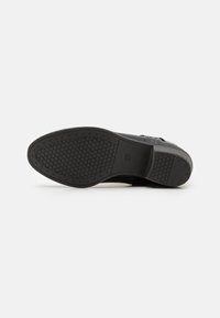 Semelle de chaussure en caoutchouc noir avec un motif en nid d'abeille texturé, présentant un bord lisse et un léger talon. Pas de marque ou d'accents visibles.