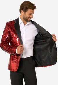 Sarkans sequīns uzvalks ar melniem kātiem, ar satīna iekšpusi un vairākiem kabatām. Valkāts atvērts, atklājot baltu krekls zem tā.