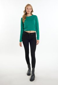 Maglione verde corto realizzato in materiale soffice, abbinato a jeans neri aderenti e stivaletti neri con suola spessa.
