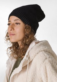 Svart stickad mössa med en slouchy design och texturerad yta, bärs med en krämfärgad fleecejacka som har huva och dragkedja.