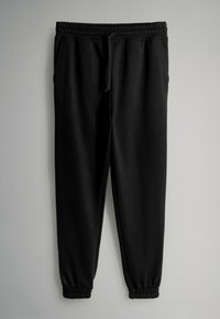 Čierne tepláky s elastickým pásom a sťahovacou šnúrkou, vybavené elastickými manžetami a bočnými vreckami, vyrobené z mäkkého, elastického materiálu.