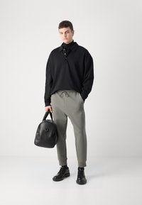 Črna polo majica z dolgimi rokavi in gumbi, sivi trenirki z vrvico, črna usnjena torba in črne čipkaste čevlje. Minimalističen dizajn.