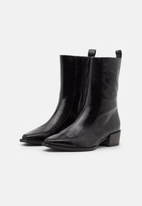 Botas de cuero negras hasta el tobillo con punta afilada, cremallera lateral, acabado liso y tacón bajo apilado para mayor estabilidad.