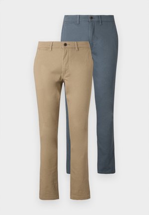 Due paia di pantaloni a gamba dritta: uno in khaki e uno in blu scuro. Realizzati in cotone; presentano una cintura e chiusura con bottone.