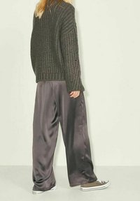 Oversized dark green knitted sweater with ribbed texture, paired with loose satin gray pants and brown sneakers, viewed from behind.