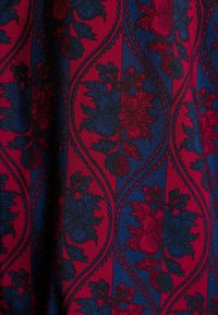 Tkanina w pionowe czerwono-niebieskie paski z naprzemiennymi wzorami kwiatowymi, zamkniętymi w falistych diamentach z czarną obwódką.