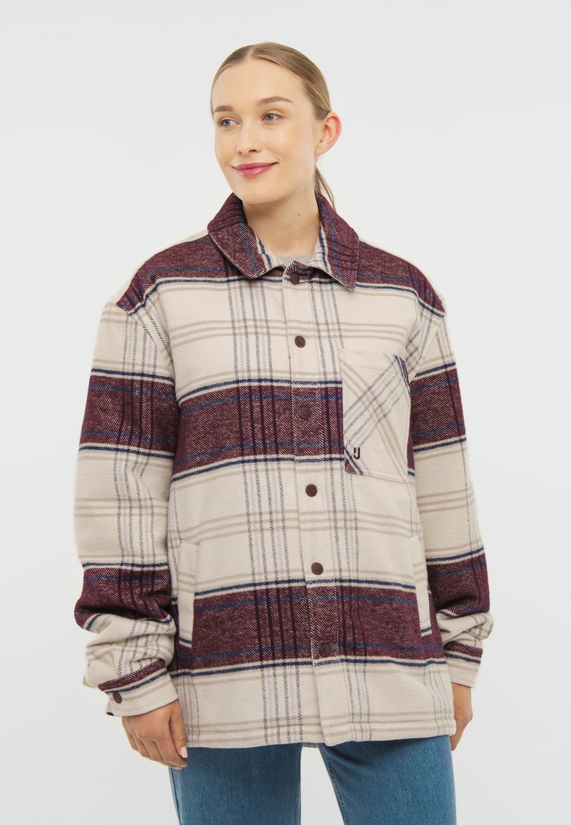 Jachetă cămașă cu mânecă lungă, de culoare bej, cu un model în carouri maronii și albastre, cu închidere cu nasturi și buzunar pe piept cu capac. Material moale și călduros.