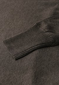 Pullover in maglia grigio scuro con polsini a coste. La texture è liscia con una finitura morbida, evidenziando la qualità pregiata del tessuto.