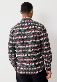 Pitkähihainen paita, jossa musta pohja ja vuorottelevat kuviot valkoisista hahmoista, punaisista karkkikepeistä ja vihreistä kuusista. Puuvillamateriaalia.