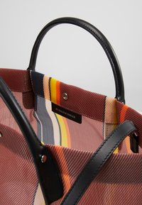 Tote bag met zwarte leren handvatten, met een meerkleurige gestreepte stoffen binnenkant in oranje, rood, marineblauw en beige met een merklabel.
