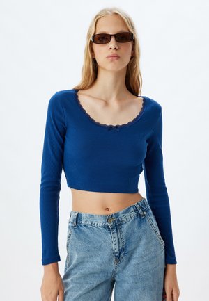 Top crop a maniche lunghe blu con una texture a coste e collo a scallop. Abbinato a jeans in denim sbiaditi a vita alta.
