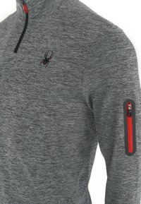 Miesten harmaa neljänneksellä vetoketjulla varustettu pusero, jossa on teksturoitu kangas. Siinä on punainen vetoketjullinen tasku hihassa ja pieni musta hämähäkkilogo rinnassa.