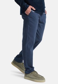 Pantalones de algodón ligeros de color azul marino con corte recto, con bolsillos laterales y una textura suave. Combinados con zapatos tipo slip-on de ante gris.