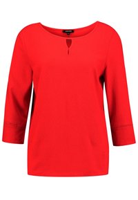 Haut rouge à manches 3/4 avec un col rond et une petite découpe en forme de clé. Texture lisse avec des détails en dentelle aux poignets.