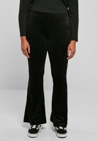 Svarta manchesterbyxor med utsvängda ben och en mjuk textur, med smal midja och en subtil lyster, ihopparade med svarta sneakers.