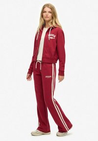 Red cotton hoodie with white "SUPER" logo, paired with matching sweatpants featuring white side stripes and logo near the waistband.