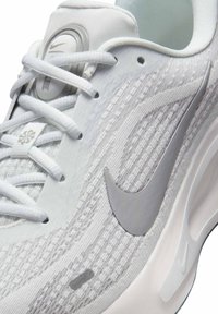 Zapatilla Nike blanca con un upper texturizado y detalles en gris, sistema de cordones redondo y un logotipo gris prominente en el lateral.