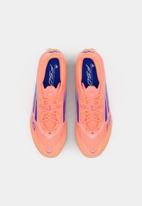 Scarpini da calcio rosa chiaro con accenti e strisce blu, caratterizzati da una parte superiore texturizzata e un design elegante. I lacci sono posizionati al centro.