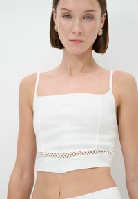 Weißes Crop-Top aus Leinen mit einem quadratischen Ausschnitt, dünnen Trägern und einem dekorativen ausgeschnittenen Spitzenpanel an der Taille.