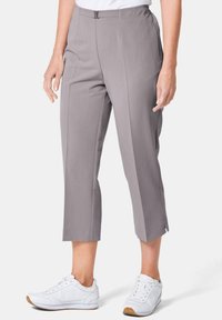 Graue, cropped Hosen mit glatter Textur, ausgestattet mit einem Bundverschluss und Falten, kombiniert mit weißen Sneakers und einem schlichten weißen Oberteil.