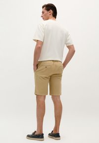 Beige shorts dengan pinggang tali dan dua kantong belakang. Dipadukan dengan kaos lengan pendek berwarna krem muda dalam potongan santai.